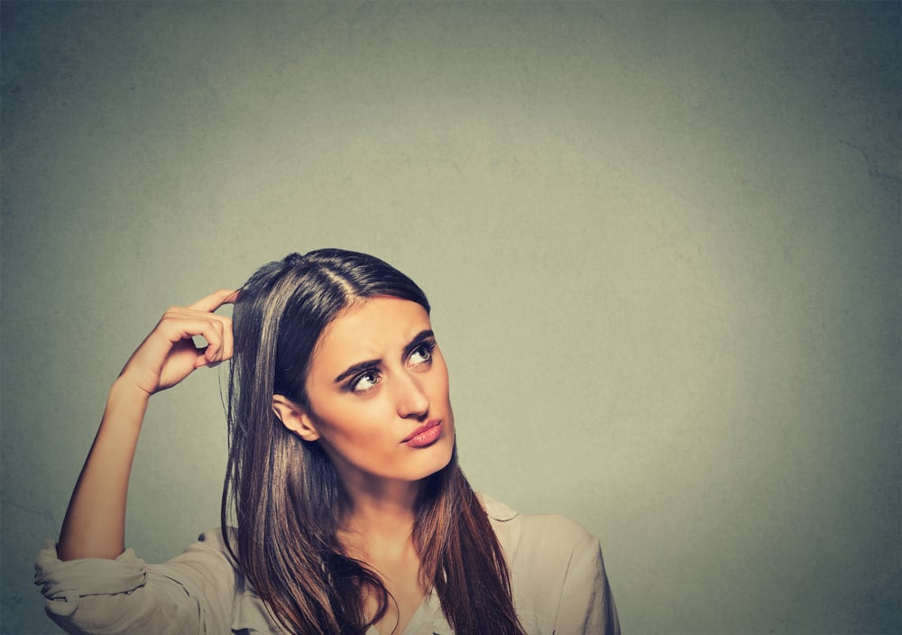 Contused thinking woman bewildered scratching her head seeks a solution isolated on gray wall background. Young woman looking up
